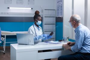 Clinic doctor holding vial of prescribed medicine while talking to retired patient about treatment. Clinic specialist doctor conversating with senior man about coronavirus epidemic outbreak