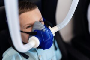 Small kid breathing through oxygen mask while having therapy in hyperbaric chambe