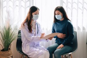 asian-doctor-visit-examines-young-adult-woman-hospital-with-stomach-ache-doctor-checking-up-consulting-health-care-wearing-mask-protect-covid19-pandemic_