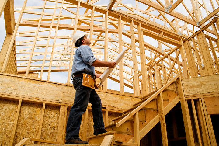 A man stands on a wooden staircase in a house that is currently under construction, observing the work around him.